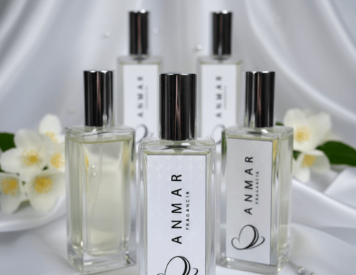 Anmar Fragancia perfume bottles on white silk fabric with jasmine flowers and pearls.