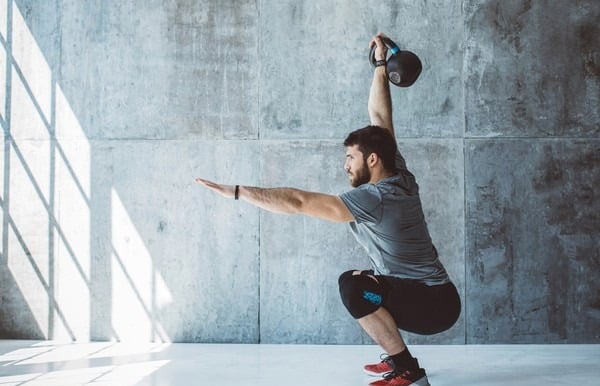 Homem vestindo roupa de academia realizando elevação do braço com Kettlebell