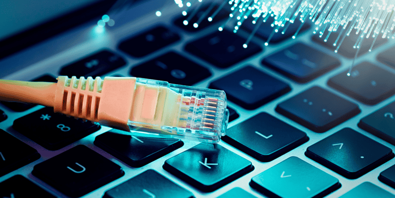 An Ethernet cable connector resting on a laptop keyboard next to glowing blue fiber optic cables.