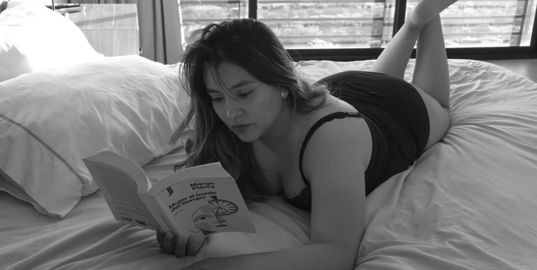 Una mujer se relaja en una cama mientras lee un libro en una foto a blanco y negr