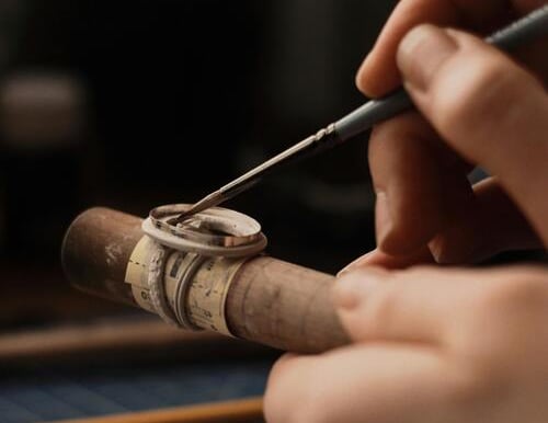 Joyero artesano pintando a mano un anillo de plata en un mandril de madera utilizando un pincel de p