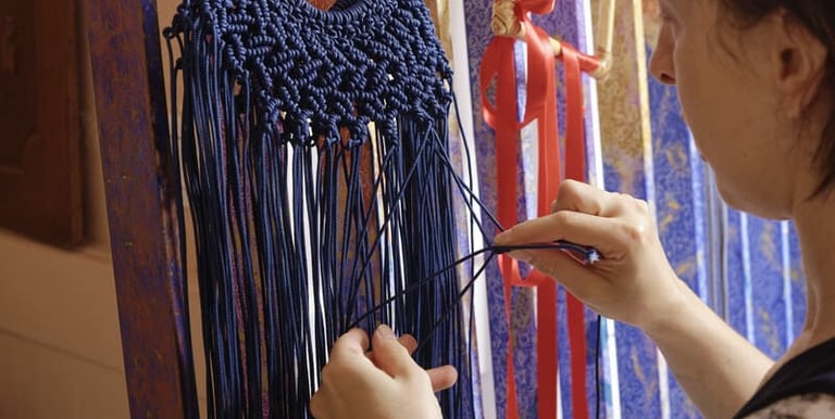 Una artesana utiliza técnicas de anudado manual para crear un tapiz de macramé azul en un telar vert