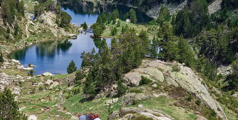 A female backpacker hiking with trekking poles near a scenic mountain lake in the Pyrenees.