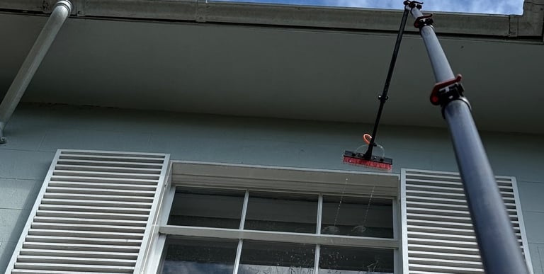 a pole with a brush head attached to it spraying a window