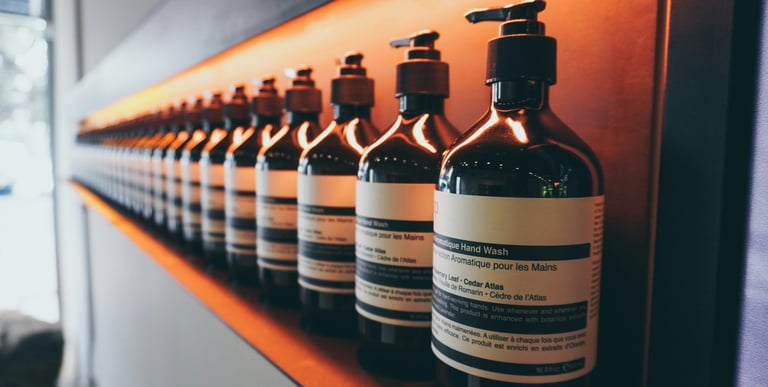 A row of Aesop aromatic hand wash glass pump bottles on a backlit wooden shelf.