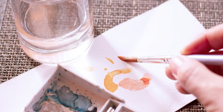 Artist painting orange watercolor strokes on paper with a brush and water glass.
