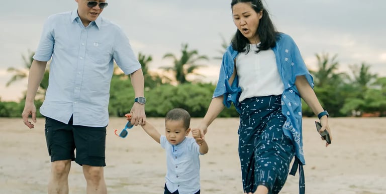 Parents walking hand in hand with their son along the shoreline during a family photography session at Nusa Dua Beach Bali