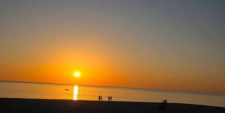 Atardecer en playa a contra luz se ve una lancha y varias personas