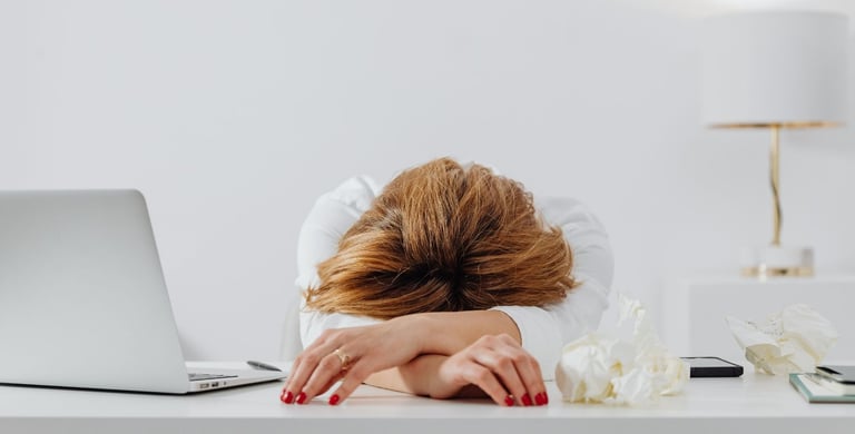 a woman with her head in her hands, sitting at a desk with a laptop