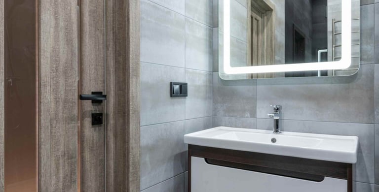 Photo of a modern bathroom vanity with illuminated mirror and grey tiled