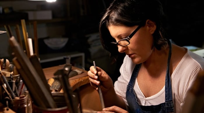 Artesana mujer utilizando herramienta profesional para hacer joyería.