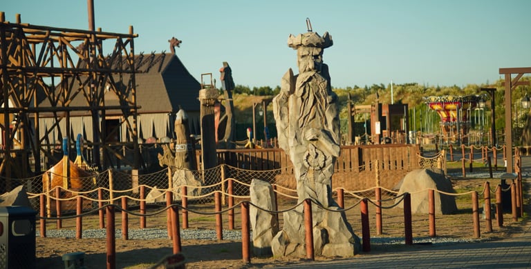 Tall stone Viking warrior statue at a Nordic-themed adventure park with wooden structures and ships.