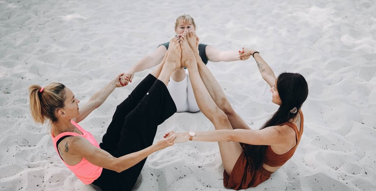 Photo des trois professeurs assises, se tenant les mains en cercle, les pieds connectés vers le ciel