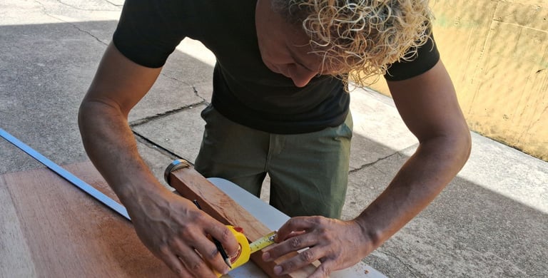 A carpenter with curly blonde hair uses a yellow measuring tape on a wooden plank for a DIY project.