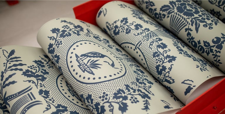 Rolls of vintage blue and white toile wallpaper with floral and bird patterns in a red rack.