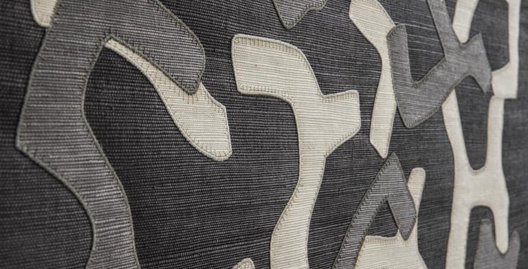 Close-up of grey and white textured fabric with abstract appliqué shapes for modern interior design.
