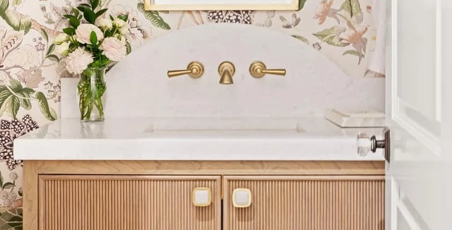 Elegant bathroom vanity with floral wallpaper, gold mirror, and marble countertop.