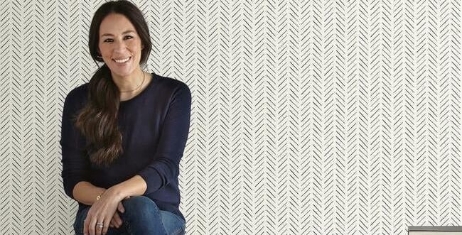 Joanna Gaines sits on a black bench against black and white herringbone peel and stick wallpaper.