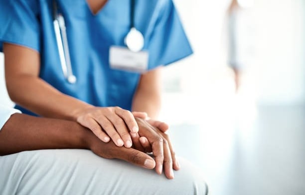 A nurse gently holds a patient's hand, providing comfort and support in a healthcare setting.