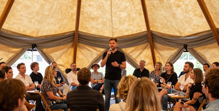 A speaker addresses a seated audience during a corporate retreat workshop inside a large canvas tipi tent.