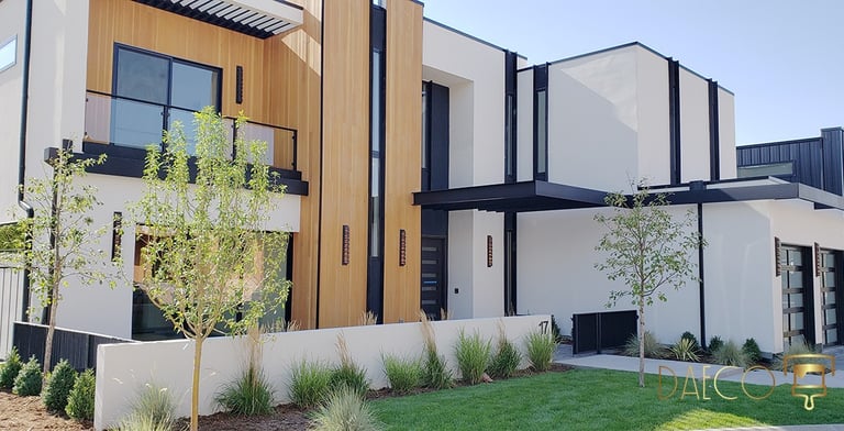 Modern luxury home exterior with wood paneling, white stucco, and contemporary landscaping.