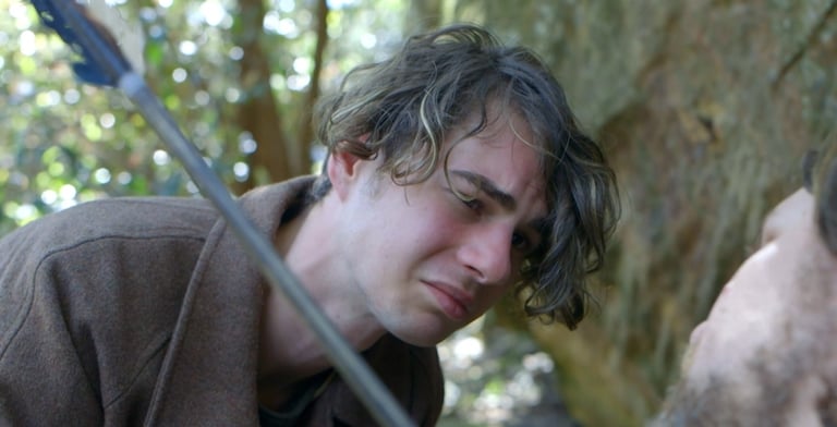 a man in a brown jacket is holding a sword