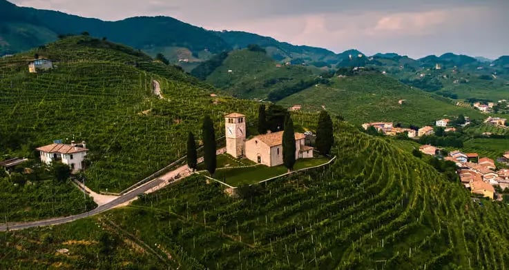 Old stone church with cypress trees surrounded by lush Prosecco vineyards in Veneto region