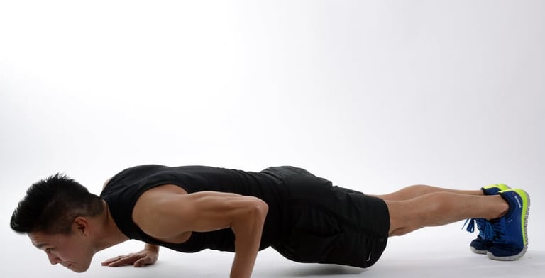 A person with lean arm muscles is in plank position in a white room.