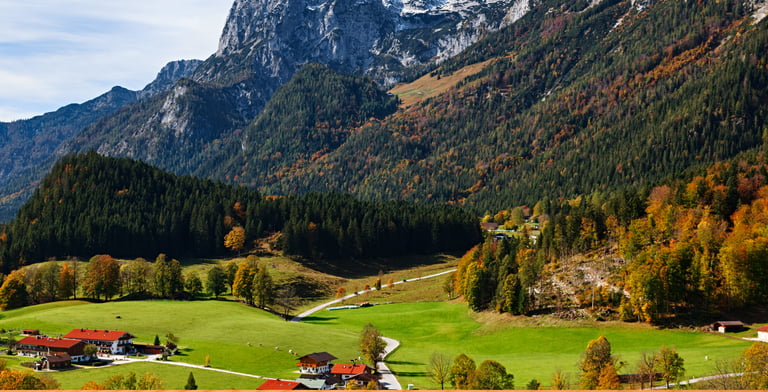 Scenic landscape of an Alpine village in autumn with traditional houses, green meadows, and rugged mountains.