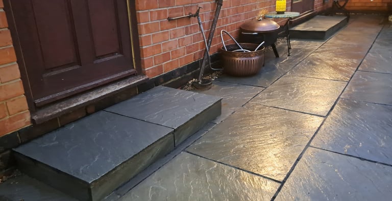 Natural grey sandstone patio tiles and doorstep leading to a brick house with a copper fire pit.
