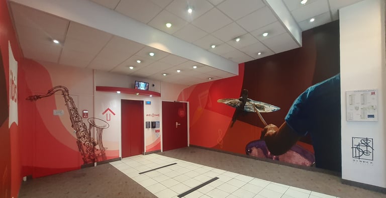 Modern ibis hotel lobby featuring red elevator doors and vibrant musical wall murals.