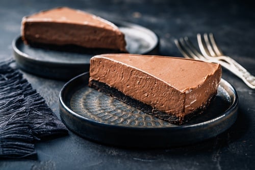 Two slices of rich chocolate mousse cake with a dark cookie crust on black ceramic plates.