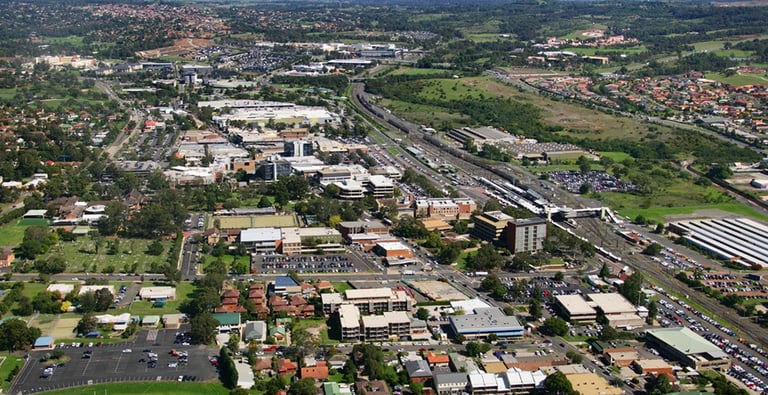 Aerial view of Campbelltown NSW showing urban buildings, railway lines, parks, and surrounding