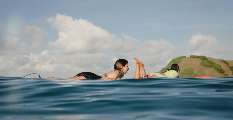 Two women lying on surfboards paddling out to the lineup in the ocean.