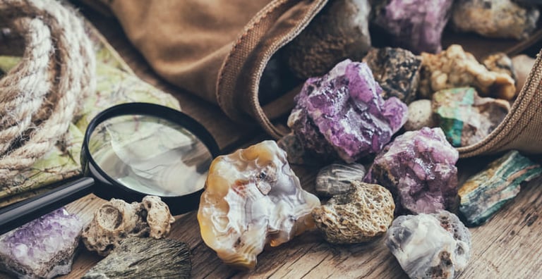 Cristales en bruto de amatista morada y ágata derramados de una bolsa de lona, junto a una lupa