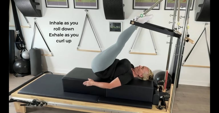 a woman laying on her back working her spine mobility with the push through bar on the Pilates Tower