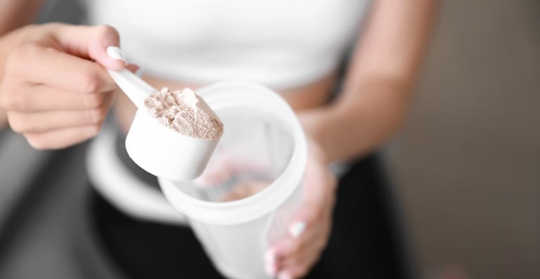 Mulher de top branco segura um dosador com suplemento em pó, tipo whey protein, acima de um shaker