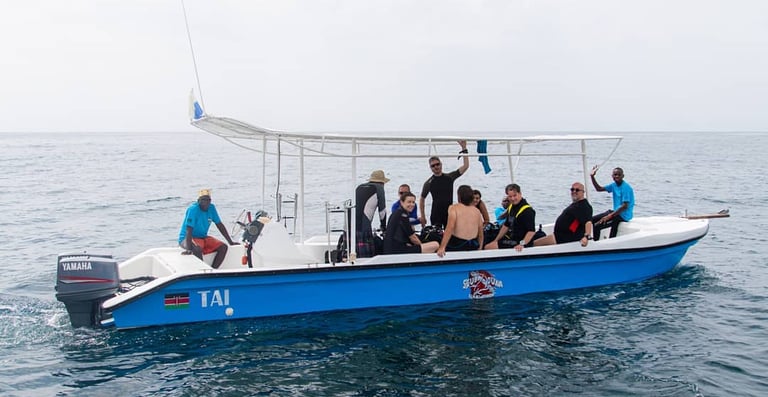 Scuba divers in wetsuits preparing for a dive on a blue boat in the Indian Ocean.