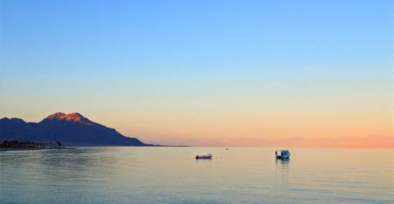 Sunset over the quiet Red Sea with Saudi Arabian mountains and boats viewed from Bedouin Star Sinai