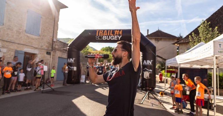 a man in a black shirt speaking with a microphone in a sport event, in front of the starting line