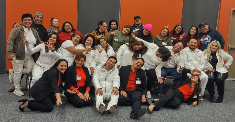 A diverse group of cheerful coworkers posing for a team photo in an office with an orange and grey wall.