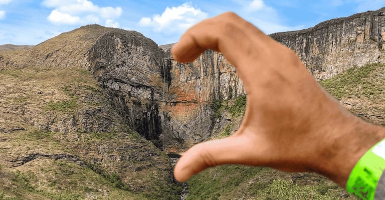 Cachoeira do Tabuleiro em Minas Gerais vista entre paredões rochosos e emoldurada por uma mão