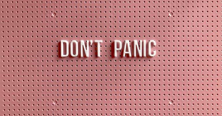 White 3D letters spelling Don't Panic on a textured pink pegboard background.
