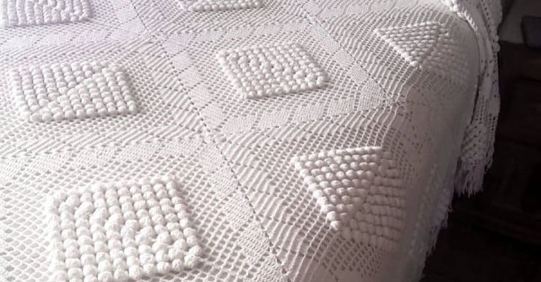 Colcha blanca vintage de ganchillo con patrones geométricos de punto texturizado sobre una cama.