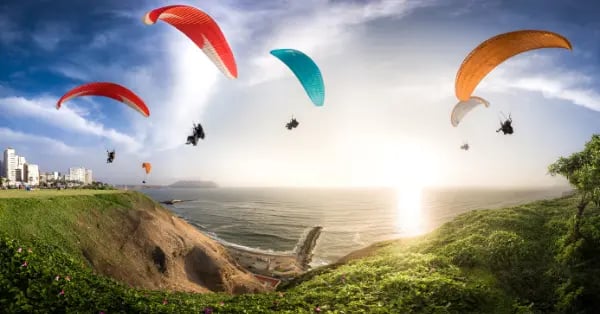 Paragliders flying over the Miraflores cliffs and Pacific Ocean in Lima, Peru during a bright sunset.