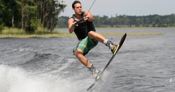 Athletic man performing a wakeboarding jump on a sunny lake with water spray.