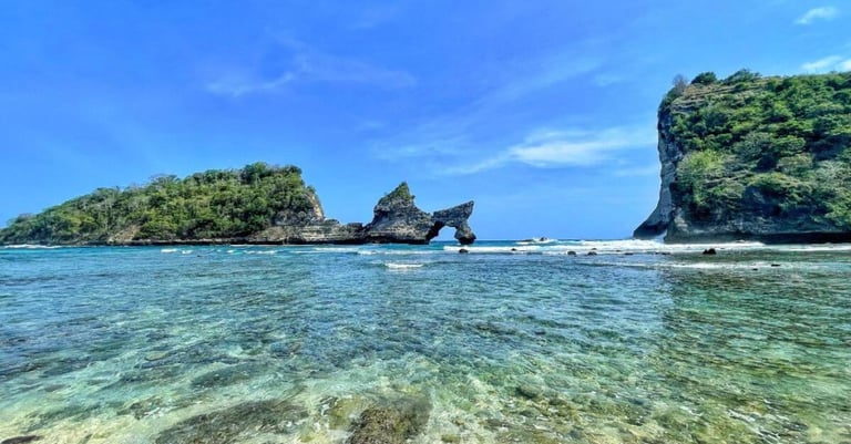 two women walking into turquoise ocean on a white sandy beach with limestone cliffs and lush green islands under blue sky