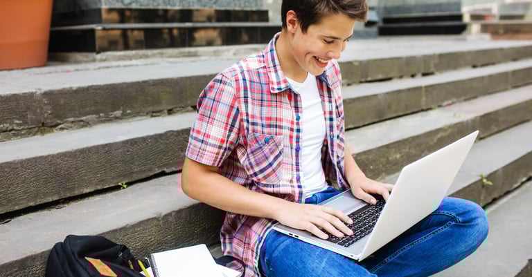 estudiante con camisa roja y pantalon azul sonriendo mientras usa una laptop para la escuela
