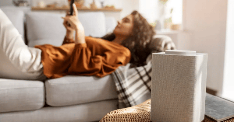 Mujer sentada en un sillón viendo su celular con un purificador de aire en primer plano