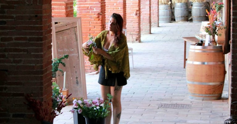 Estelle arrangeant des fleurs séchées dans des seaux sous une galerie en briques avec des arches